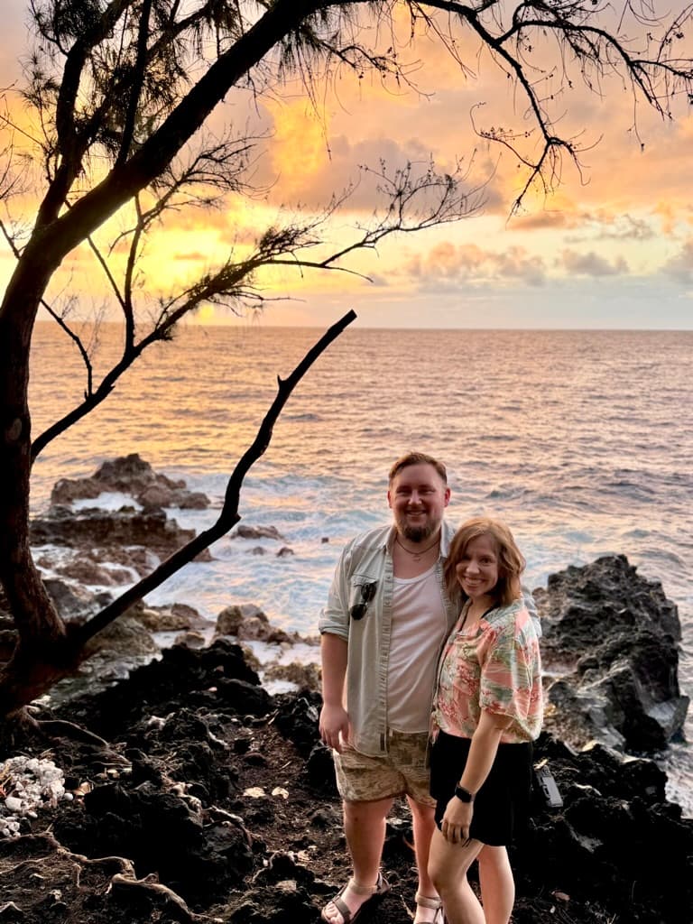 Kate and Matt on a rocky shoreline beneath tree branches.