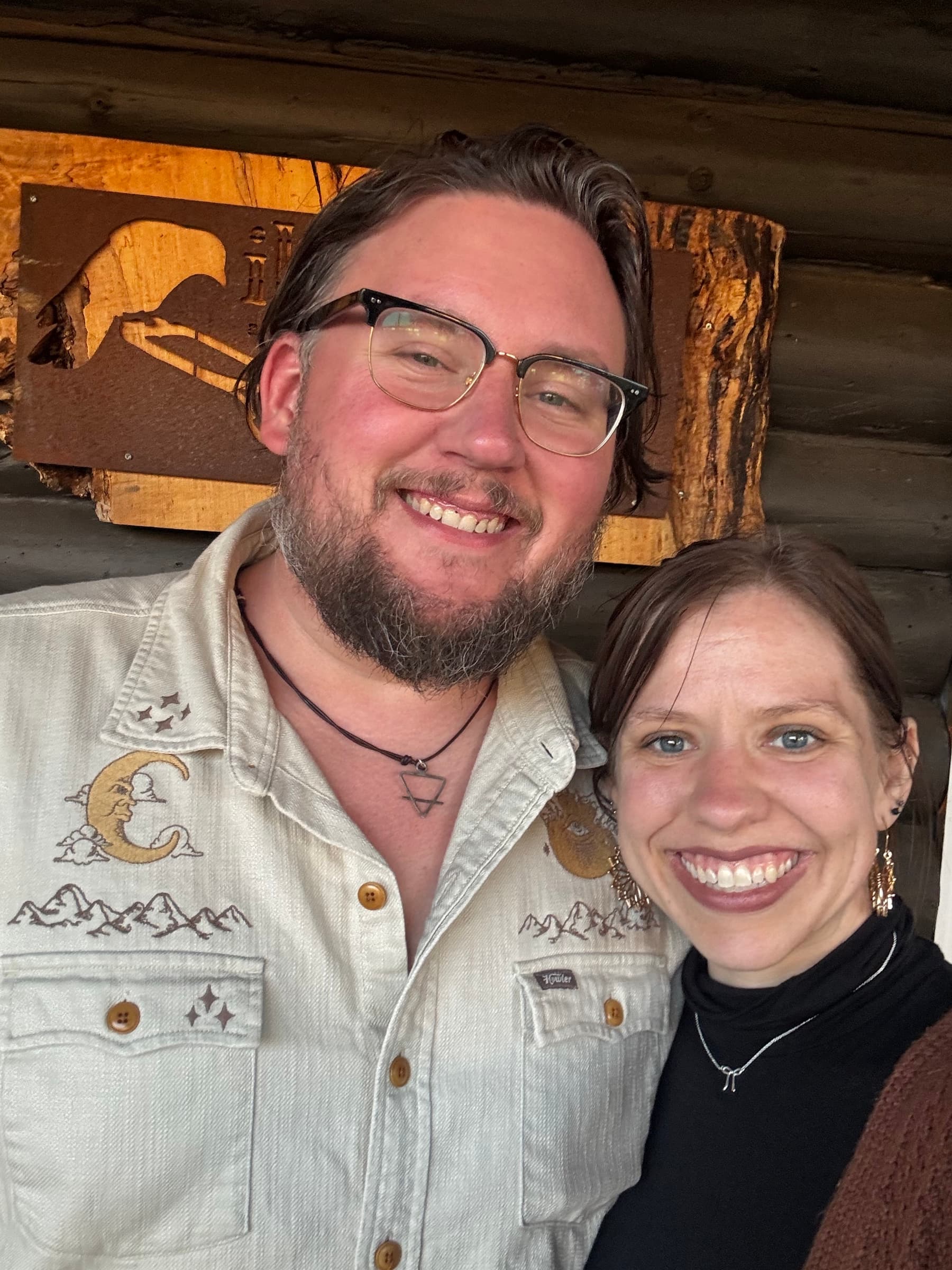 Kate and Matt smiling together in front of a dark wooden wall.